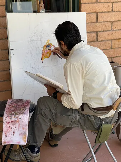 An artist paints on a canvas outdoors.