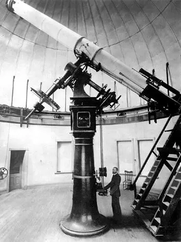 Black and white historic photo showing a large telescope inside a dome with a person standing next to it.