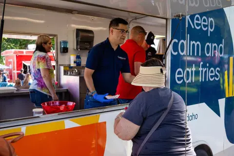 People working inside a food truck serve a customer.