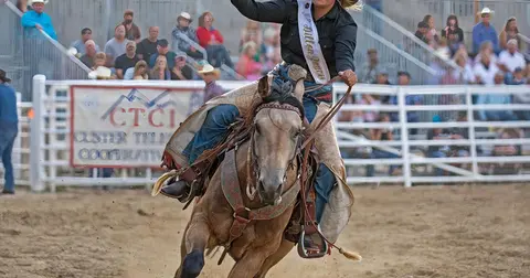 A rider on a horse racing across a rodeo arena.