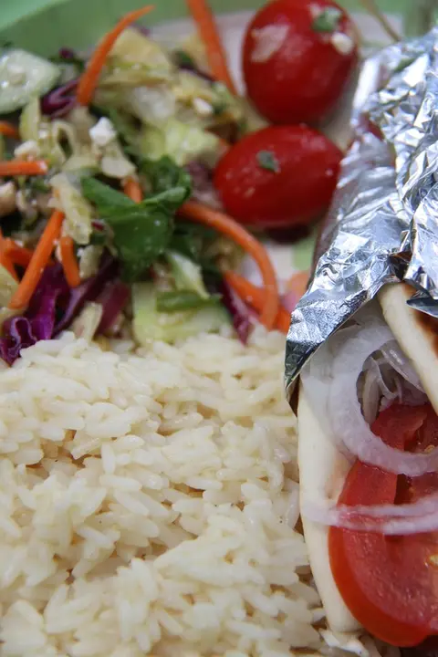 A plate of food including rice, salad, tomatoes, and a wrap in foil.