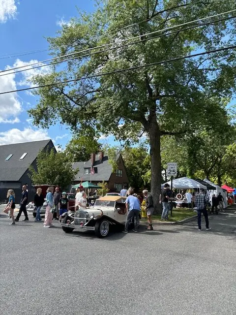A street scene with people gathered around vintage cars and tents.
