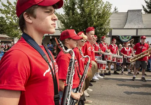 A marching band in red shirts stands on a street.
