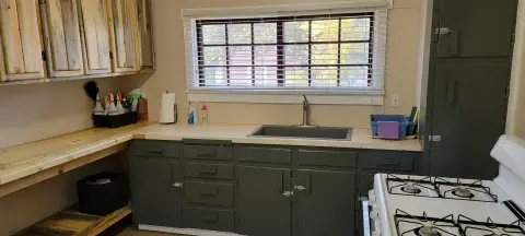 An interior shot of a rustic kitchen with grey cabinets and a window above the sink.