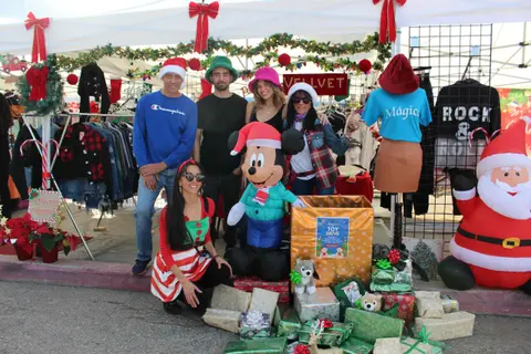 A group of people posing with holiday decorations and a toy drive box.