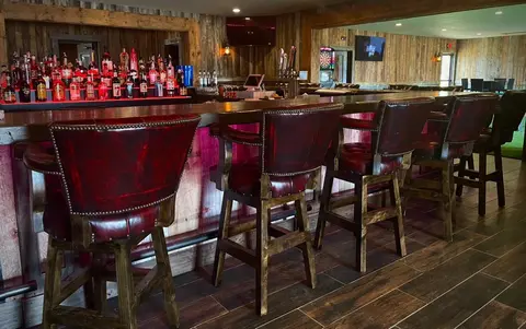 An interior view of a rustic bar with wooden walls and red leather bar stools.