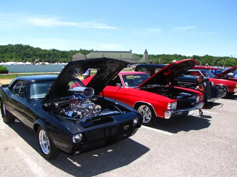 A row of classic cars parked with their hoods open at an outdoor car show.