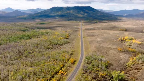 A long straight road stretching toward distant mountains through a valley with trees.