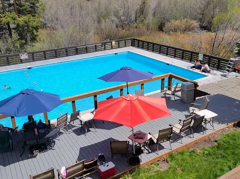 An outdoor swimming pool surrounded by a wooden deck with umbrellas and chairs.