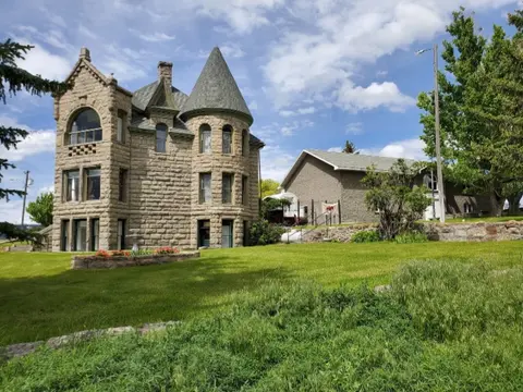 Exterior view of a historic stone building with a round turret and grassy lawn.