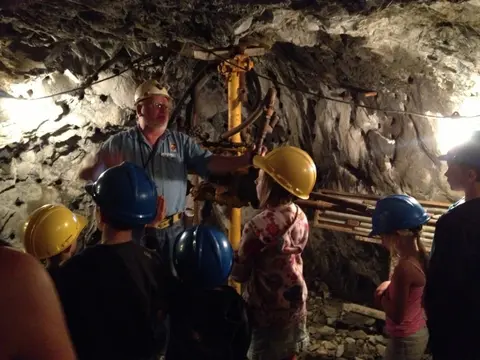 A guide talks to children wearing hard hats inside a mine.