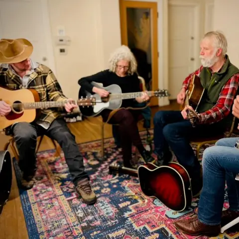 Four people are playing acoustic guitars indoors together.