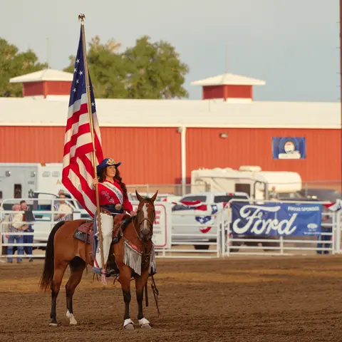 A woman on horseback holds an American flag in an arena.