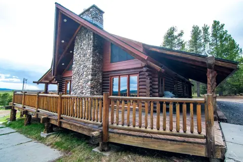 A log cabin with a stone chimney and large wooden deck.