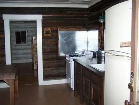 An interior view of a rustic log cabin kitchen with a stove and refrigerator.