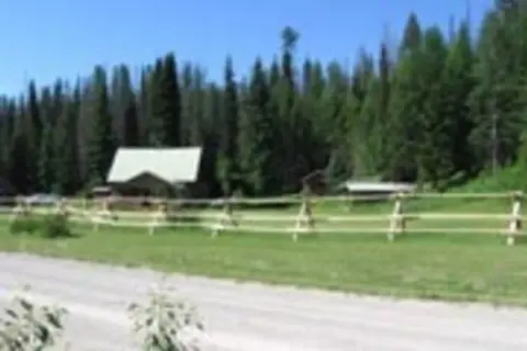 A rustic cabin nestled near a dense forest with a wooden fence in the foreground.
