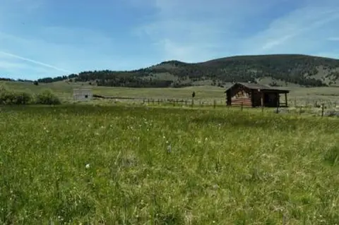 A grassy field with a small cabin and rolling hills in the background.