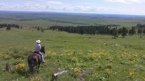 A person rides a horse across a grassy hillside overlooking a vast landscape.
