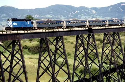 A train crosses a high trestle bridge in a mountainous landscape.