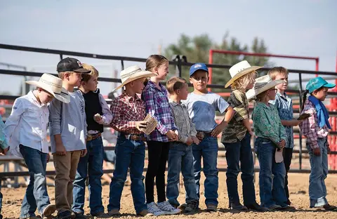 A line of children wearing cowboy hats stand in a dirt arena.