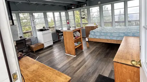 A photo showing the interior of a fire lookout cabin with a bed, kitchen area, and windows all around.