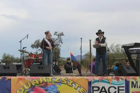 People on an outdoor stage with musical instruments and a banner.