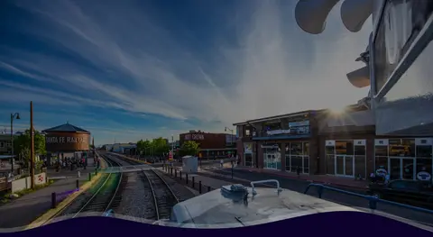 An outdoor view of a railyard and tracks alongside brick buildings under a blue sky.