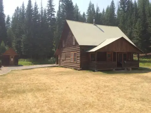 A rustic log cabin stands in a clearing surrounded by a pine forest.