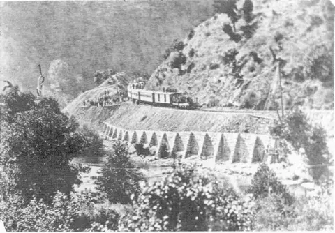 Historic black and white photograph of a train on a viaduct along a hillside.