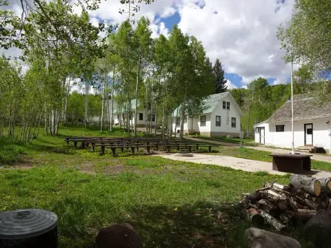 An outdoor gathering area with benches in front of several white buildings surrounded by trees.