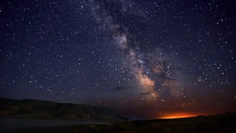 A starry night sky with the Milky Way visible above a dark landscape.