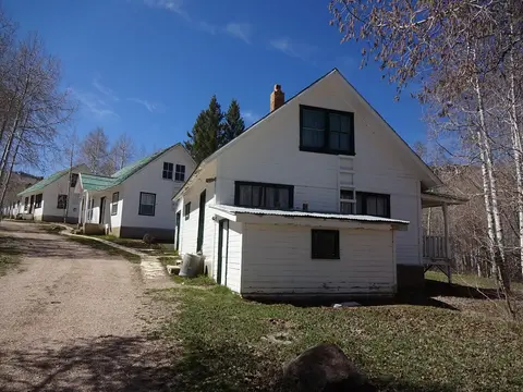 A row of white historic houses sits along a dirt road under a blue sky.