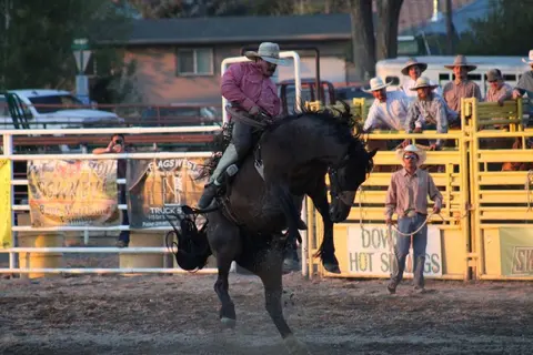 A cowboy rides a bucking horse in an arena while spectators watch.