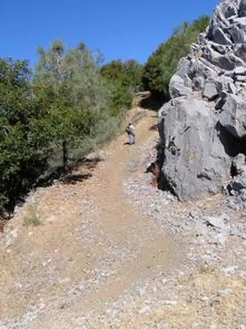 A hiker walks up a dirt trail in a rocky landscape.