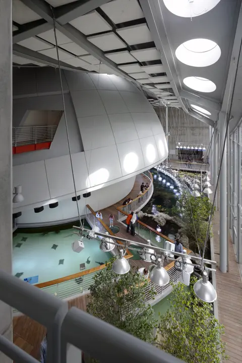 An interior view of a modern building featuring a large dome structure and exhibits with water features.