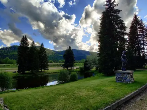 A statue stands near a pond and grassy hill with mountains in the background under a cloudy sky.