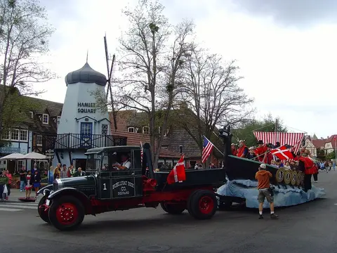 A parade float shaped like a Viking ship is towed by a vintage truck in a town square.