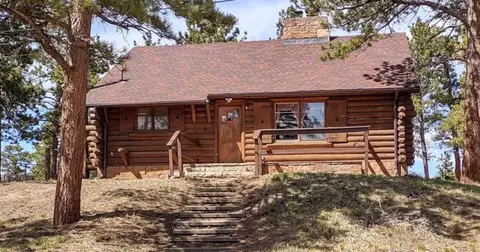 An exterior view of a wooden cabin surrounded by pine trees.