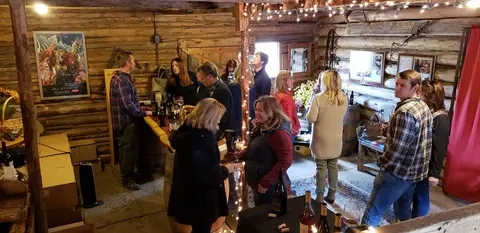 People gather inside a rustic log cabin tasting wine and socializing.