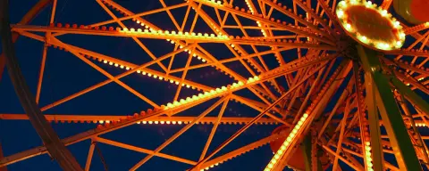 A close-up view of the illuminated metal structure of a Ferris wheel against the evening sky.
