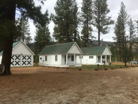 Exterior view of several white cottages with green roofs among pine trees.