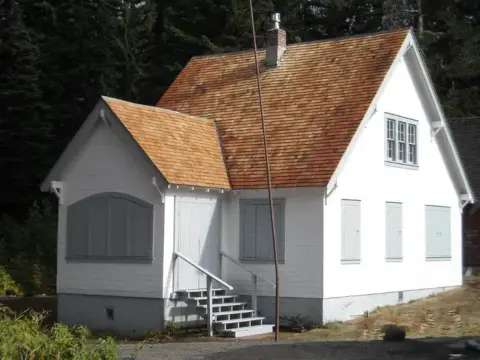 A white historic building with a wooden shingle roof and shuttered windows.