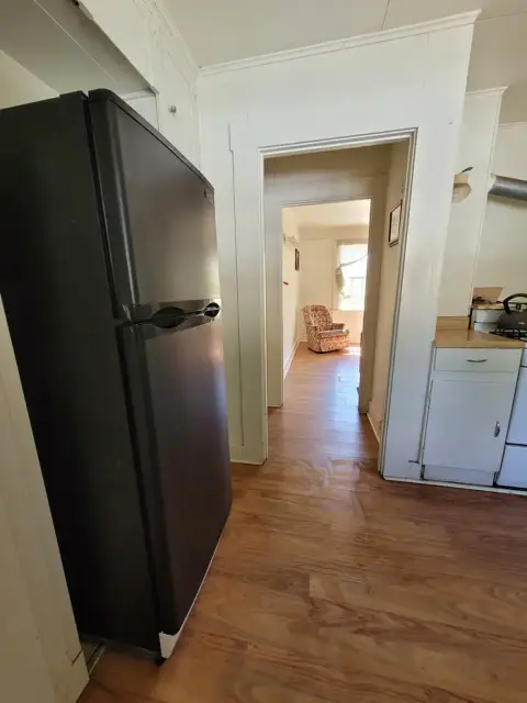 A view of the interior of a house showing a kitchen with a black refrigerator and a hallway leading to another room.