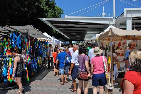 People walking through an outdoor market with vendor stalls and colorful clothing displays.
