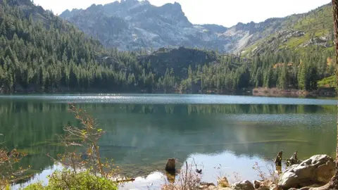 A scenic view of a calm mountain lake surrounded by trees and rugged peaks.