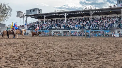 A crowded rodeo arena with riders on horseback and a crowd in the stands.