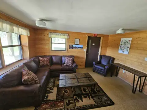 A rustic interior room with wood-paneled walls, leather couches, and a coffee table.