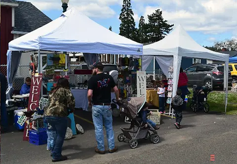 People browse crafts at booths under white tents outdoors.