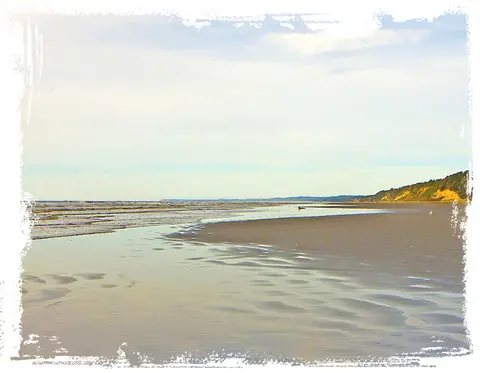 A sandy beach with gentle waves and a distant coastline under a cloudy sky.