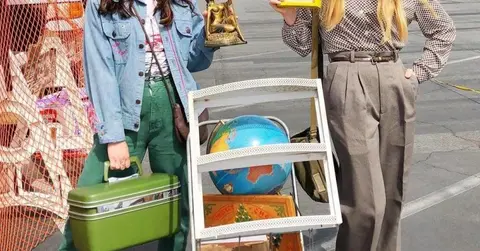 Two people pose outdoors with various secondhand items and a cart.